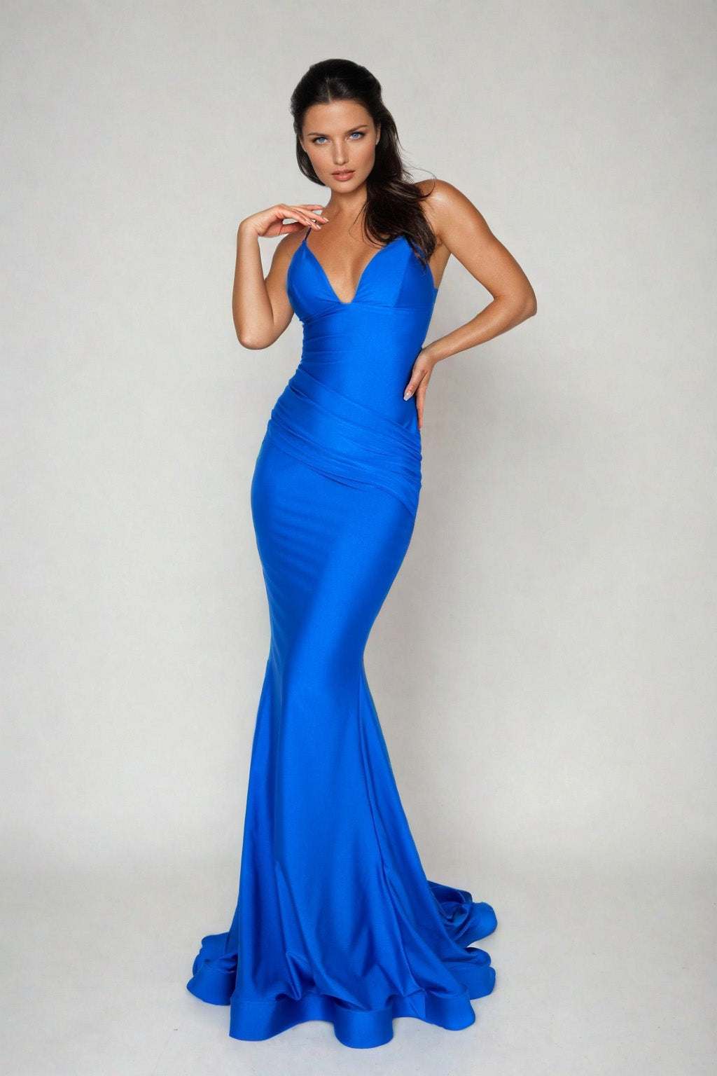 A woman poses against a plain light background in the Ruched Empire-Waist Long Mermaid Prom Dress: 6536H, featuring a bright blue hue and deep V neckline.